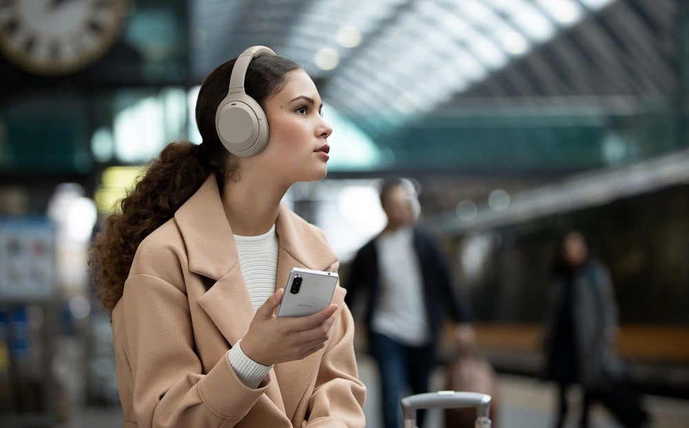 Ein Mädchen hält ein weißes Smartphone mit Sony WH1000 XM4 Kopfhörern