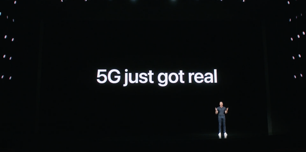 Ein Typ, der auf einer schwarzen Bühne mit 5G steht, wurde gerade auf einem Bildschirm dahinter echt angezeigt