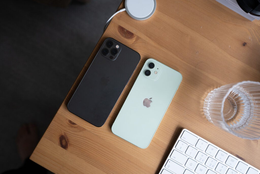 Ein schwarz-weißes iPhone 12 Pro, das verkehrt herum auf einem Holztisch liegt, Ansicht von oben