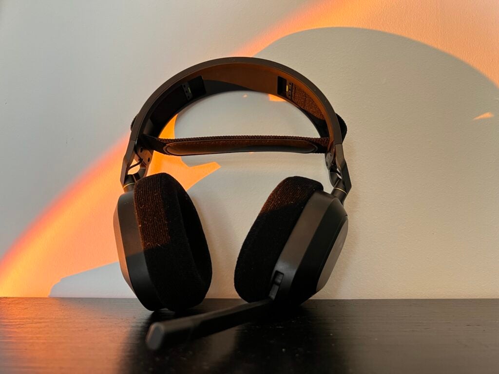 Das Corsair HS80 RGB-Headset lehnt an einer Wand auf einem schwarzen Schreibtisch