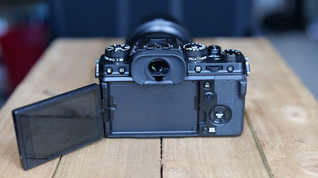 Rückansicht einer schwarzen Fujifilm XT4-Kamera, die mit aufgeklapptem Bildschirm auf einem Holztisch steht