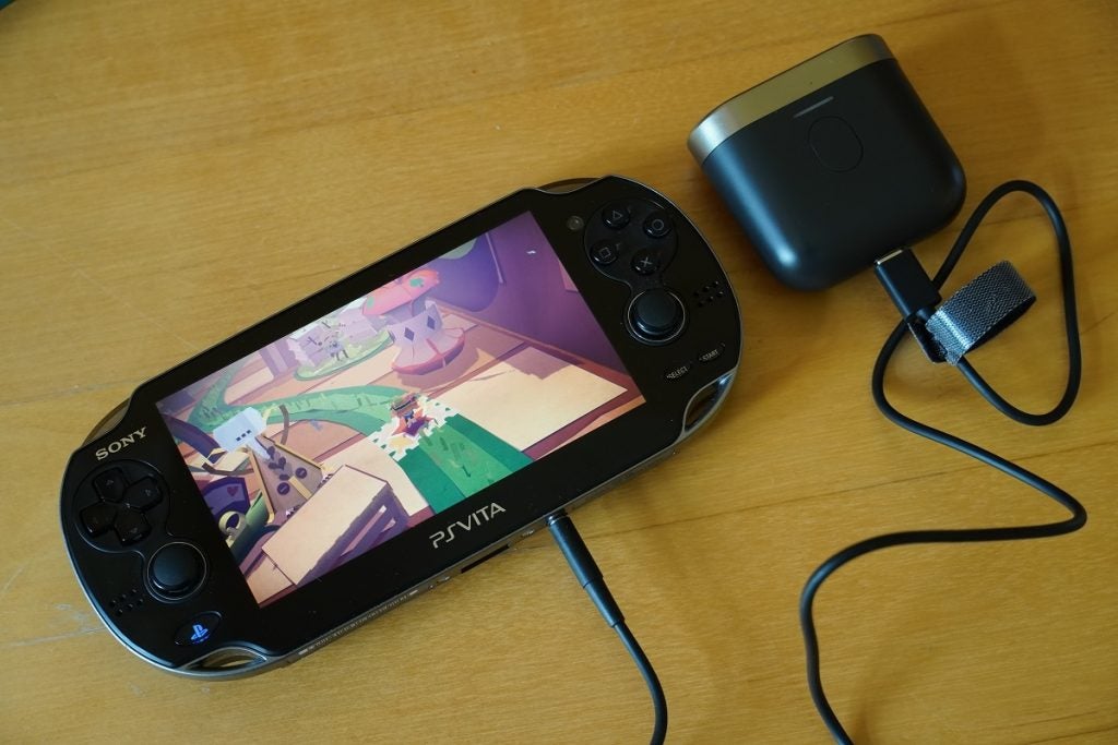 Eine schwarze Sony Playstation PS Vita, die ein Spiel mit Spielsteuerungen auf beiden Seiten zeigt, eine daran angeschlossene Buchse und das andere Ende, das an einen Lautsprecher angeschlossen ist, zeigt die Audioübertragung von Bowers und Wilkins P17